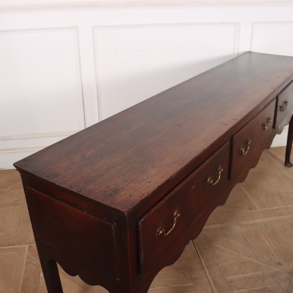 An 18th-century English oak dresser base featuring three drawers with brass handles, a scalloped apron, and cabriole legs. View VIII