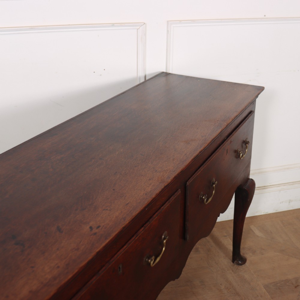 An 18th-century English oak dresser base featuring three drawers with brass handles, a scalloped apron, and cabriole legs. View IX