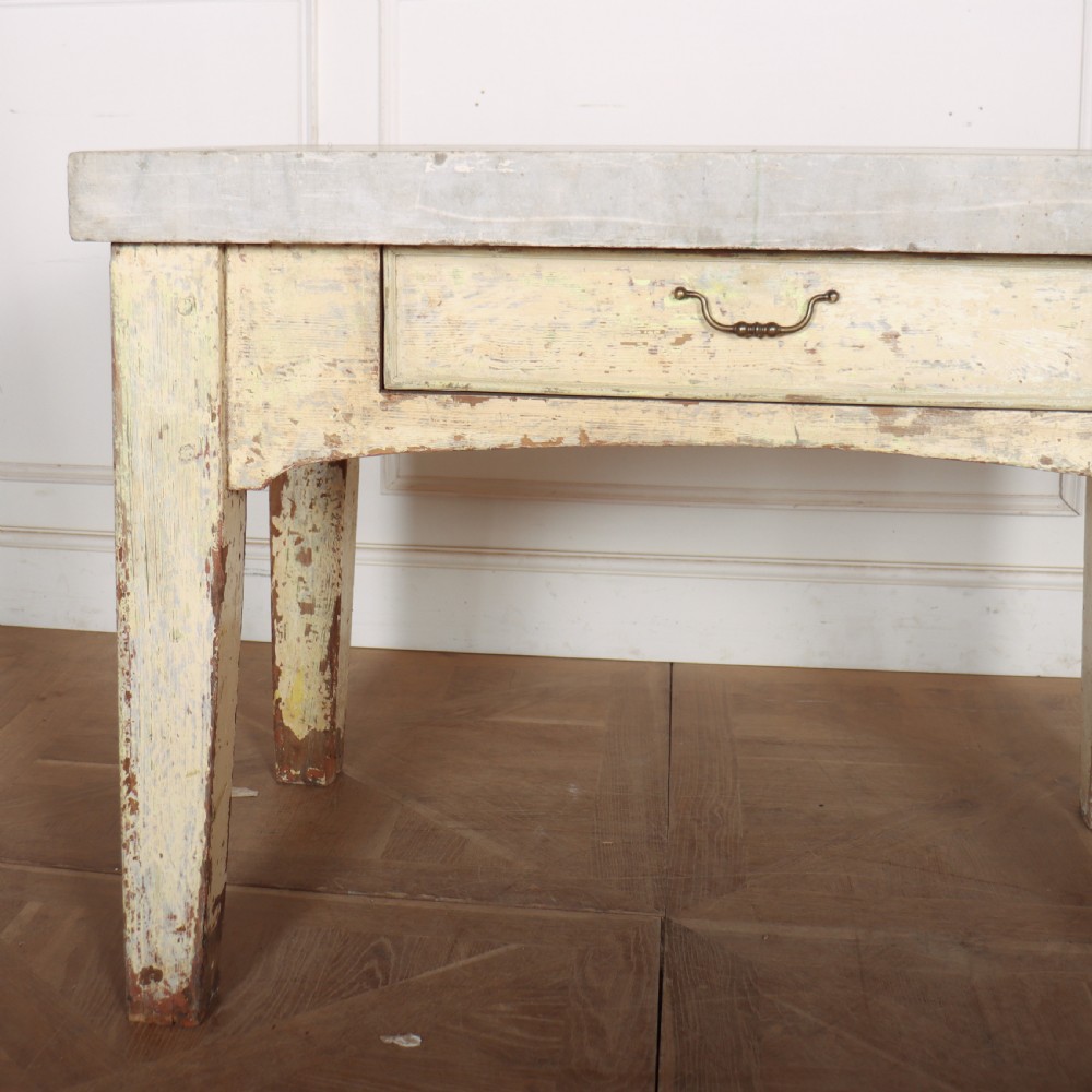 An antique pastry table featuring a distressed cream painted wooden frame, a single central drawer with a brass handle, and a thick grey metal top. View II