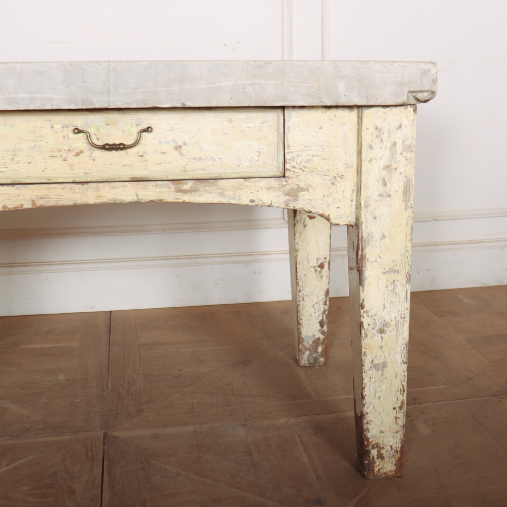 An antique pastry table featuring a distressed cream painted wooden frame, a single central drawer with a brass handle, and a thick grey metal top. View III