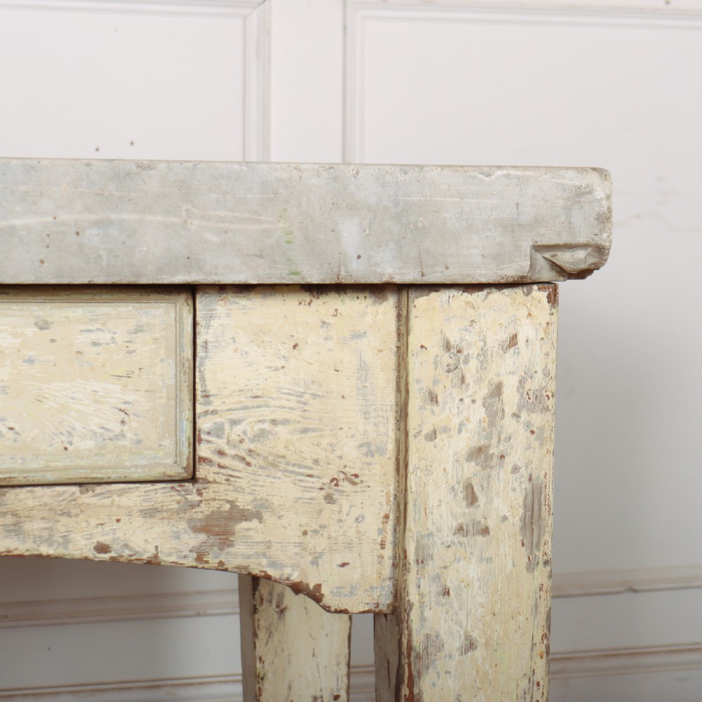 An antique pastry table featuring a distressed cream painted wooden frame, a single central drawer with a brass handle, and a thick grey metal top. View IV