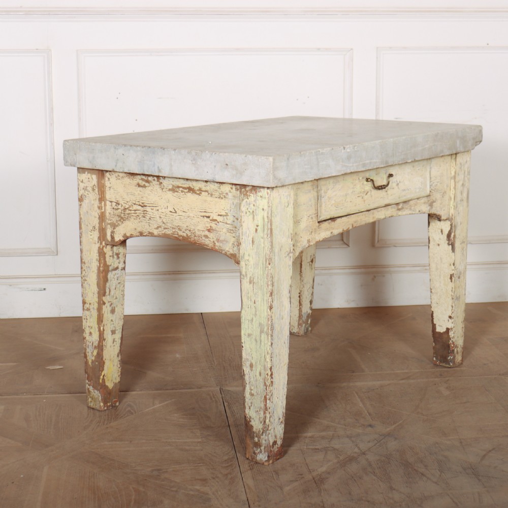An antique pastry table featuring a distressed cream painted wooden frame, a single central drawer with a brass handle, and a thick grey metal top. View VI