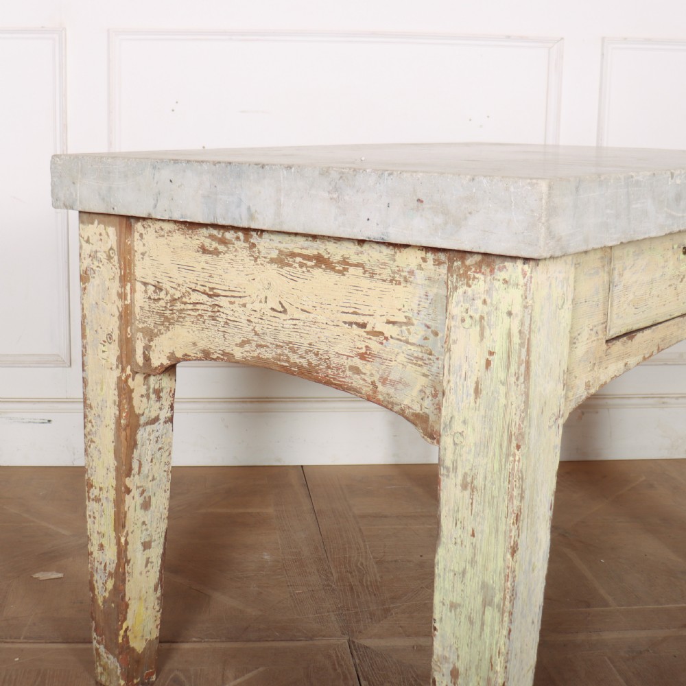 An antique pastry table featuring a distressed cream painted wooden frame, a single central drawer with a brass handle, and a thick grey metal top. View VII