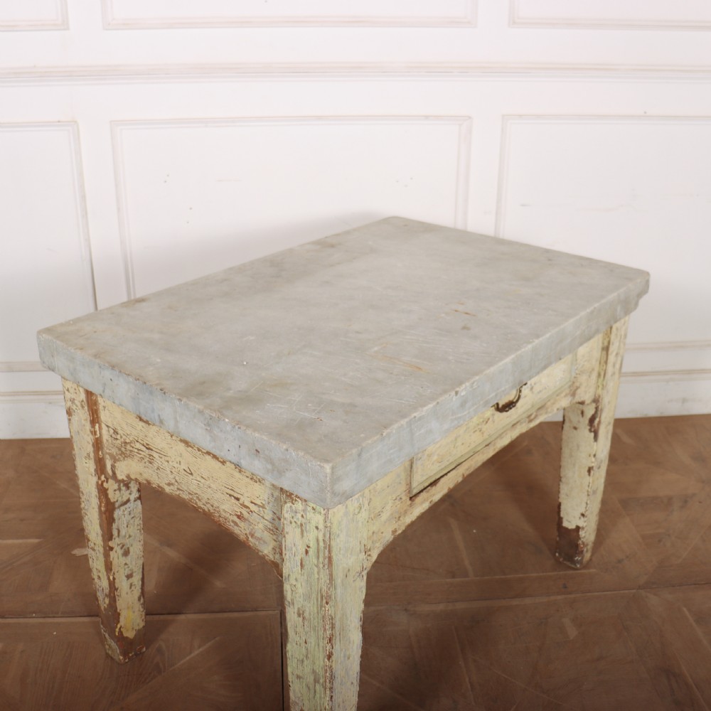 An antique pastry table featuring a distressed cream painted wooden frame, a single central drawer with a brass handle, and a thick grey metal top. View VIII