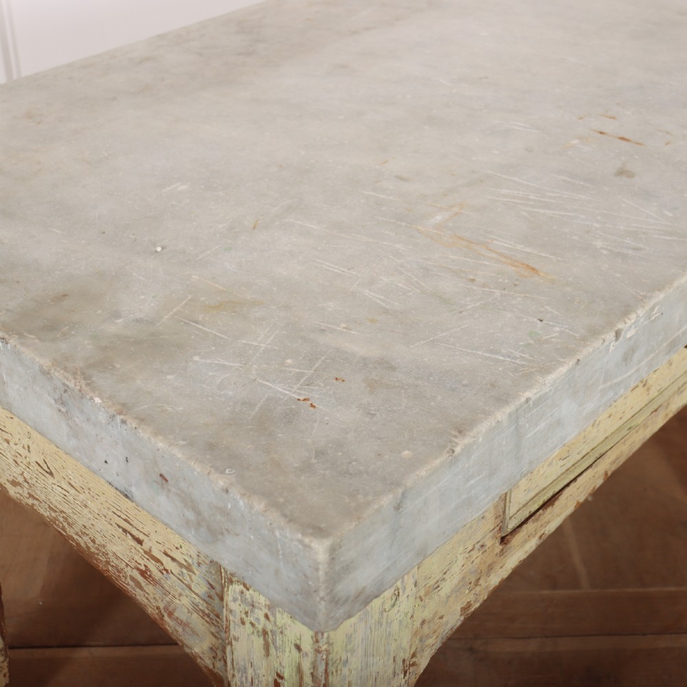 An antique pastry table featuring a distressed cream painted wooden frame, a single central drawer with a brass handle, and a thick grey metal top. View IX