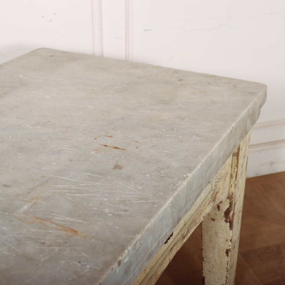 An antique pastry table featuring a distressed cream painted wooden frame, a single central drawer with a brass handle, and a thick grey metal top. View X