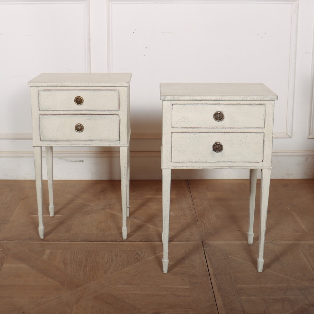 A pair of off-white painted Swedish Gustavian style bedside tables, each featuring two drawers with brass ring pull handles and slender tapered legs.