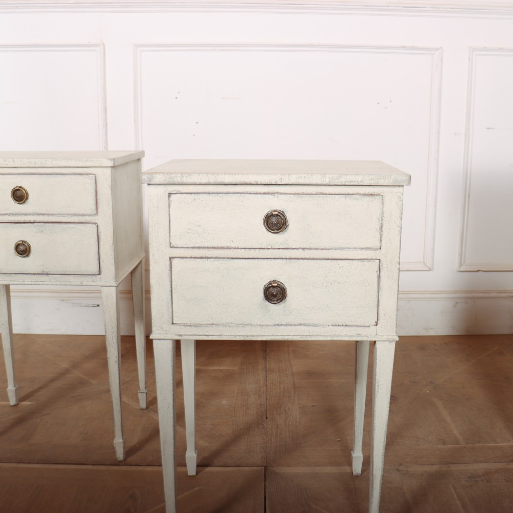 A pair of off-white painted Swedish Gustavian style bedside tables, each featuring two drawers with brass ring pull handles and slender tapered legs. View II