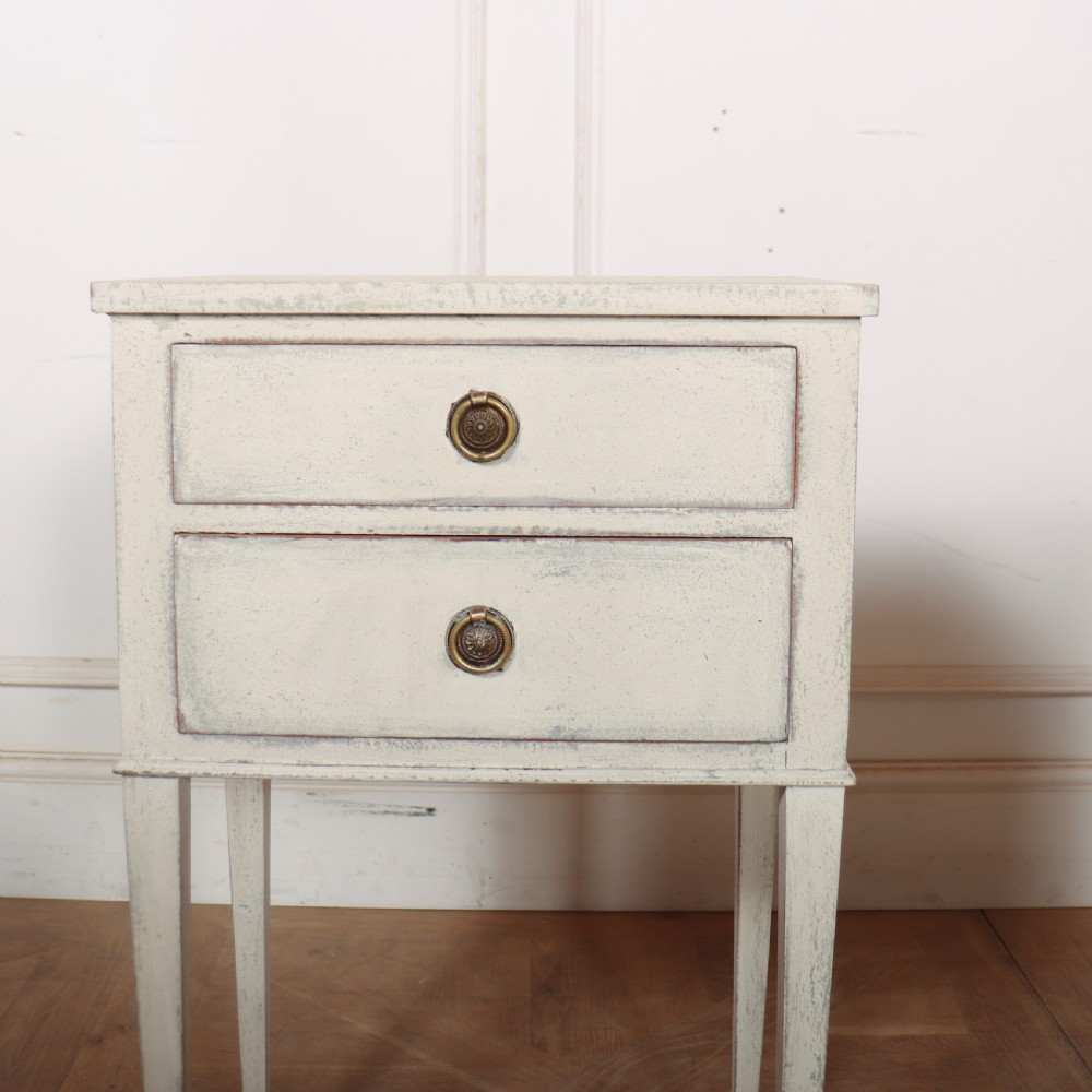 A pair of off-white painted Swedish Gustavian style bedside tables, each featuring two drawers with brass ring pull handles and slender tapered legs. View IV