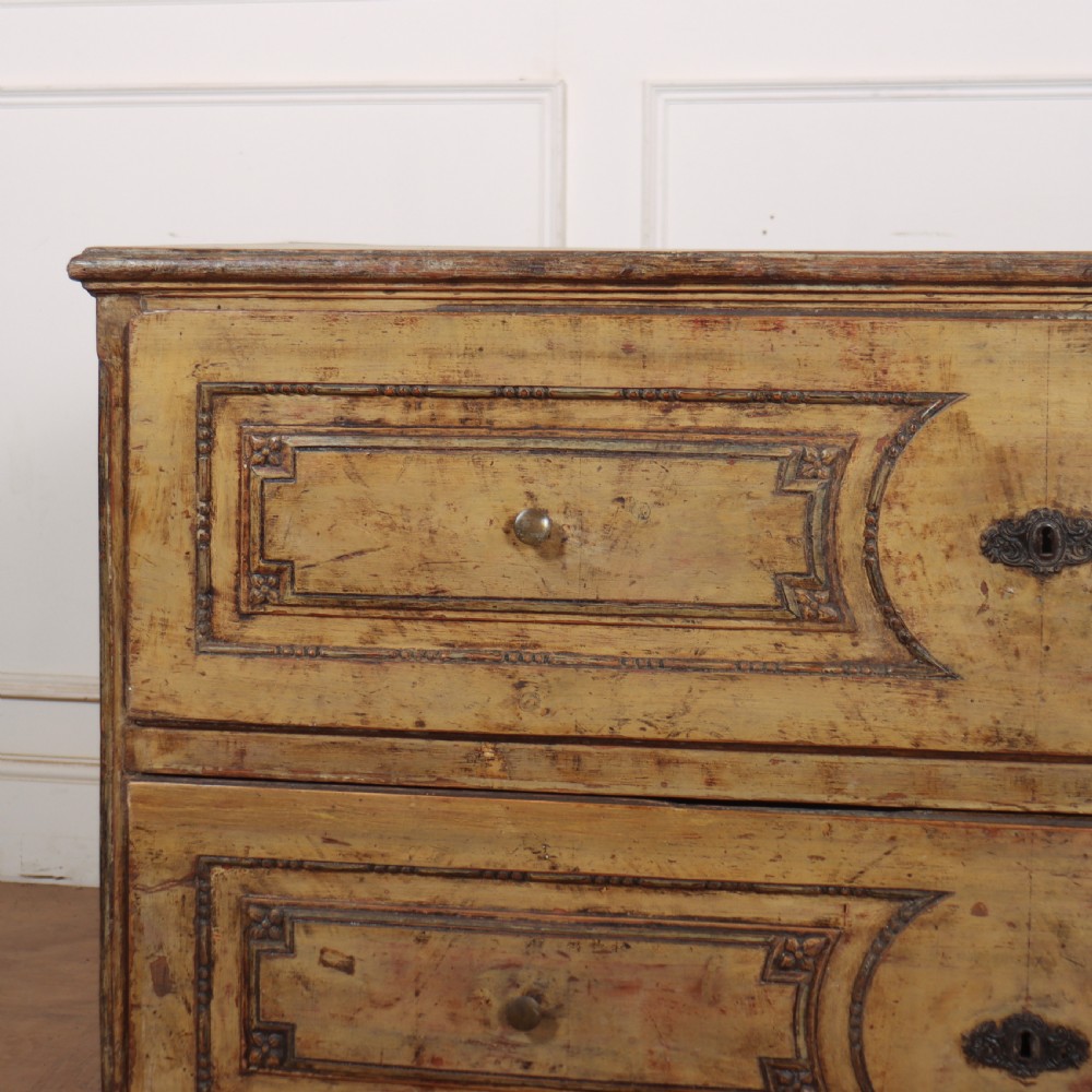 An antique two-drawer Italian commode with a muted yellow painted distressed finish, geometric panel mouldings, central brass escutcheons, and square tapered legs. View II