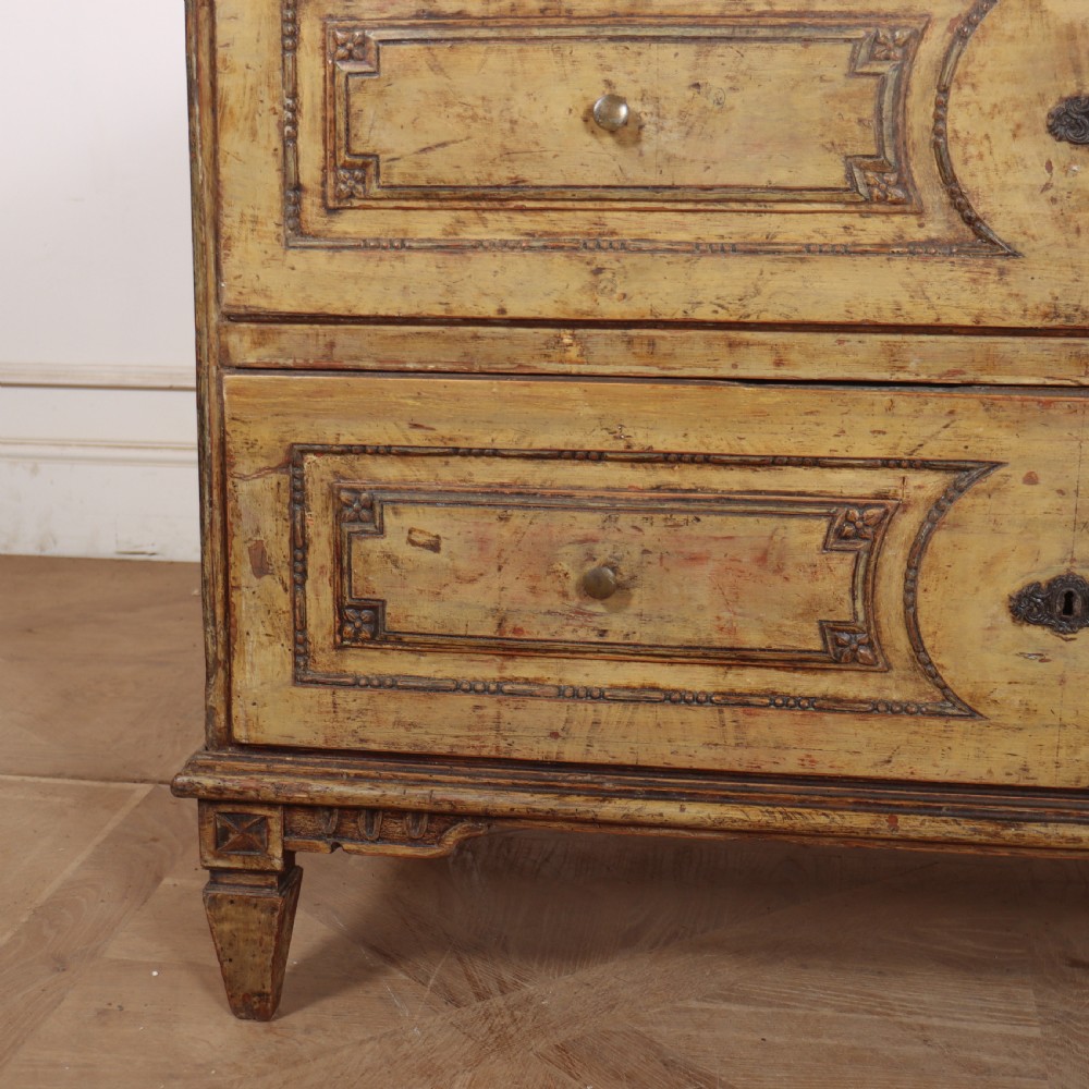 An antique two-drawer Italian commode with a muted yellow painted distressed finish, geometric panel mouldings, central brass escutcheons, and square tapered legs. View III