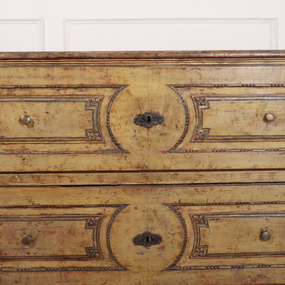 An antique two-drawer Italian commode with a muted yellow painted distressed finish, geometric panel mouldings, central brass escutcheons, and square tapered legs. View IV