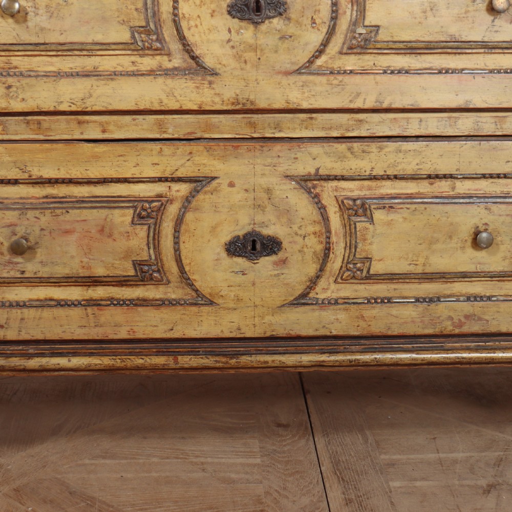 An antique two-drawer Italian commode with a muted yellow painted distressed finish, geometric panel mouldings, central brass escutcheons, and square tapered legs. View V