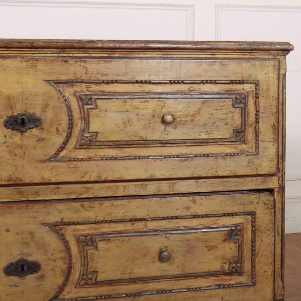 An antique two-drawer Italian commode with a muted yellow painted distressed finish, geometric panel mouldings, central brass escutcheons, and square tapered legs. View VII