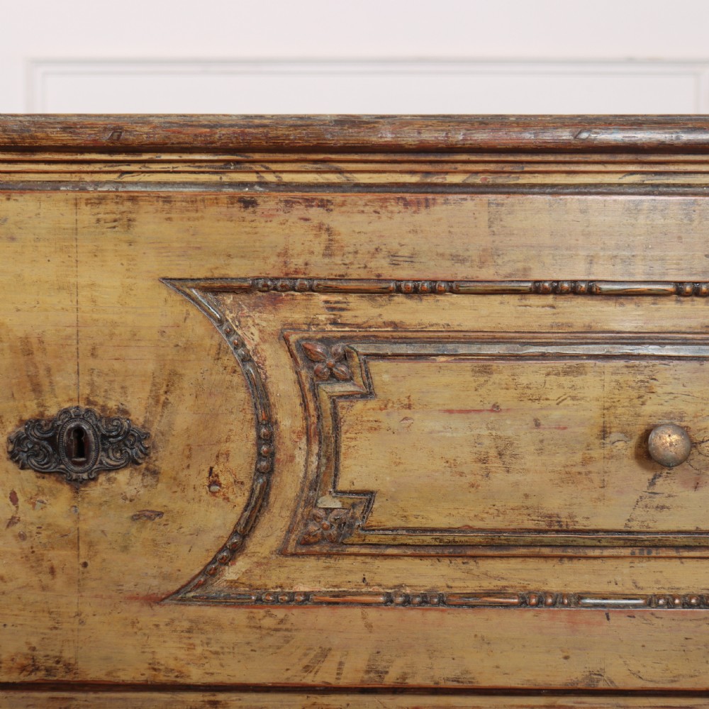 An antique two-drawer Italian commode with a muted yellow painted distressed finish, geometric panel mouldings, central brass escutcheons, and square tapered legs. View VIII