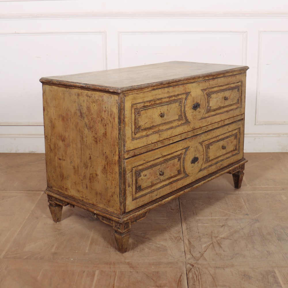 An antique two-drawer Italian commode with a muted yellow painted distressed finish, geometric panel mouldings, central brass escutcheons, and square tapered legs. View IX