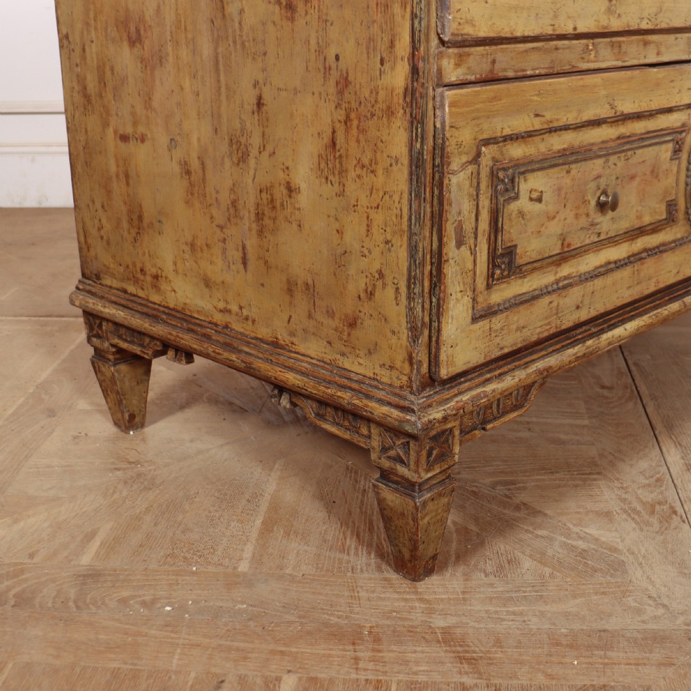 An antique two-drawer Italian commode with a muted yellow painted distressed finish, geometric panel mouldings, central brass escutcheons, and square tapered legs. View X