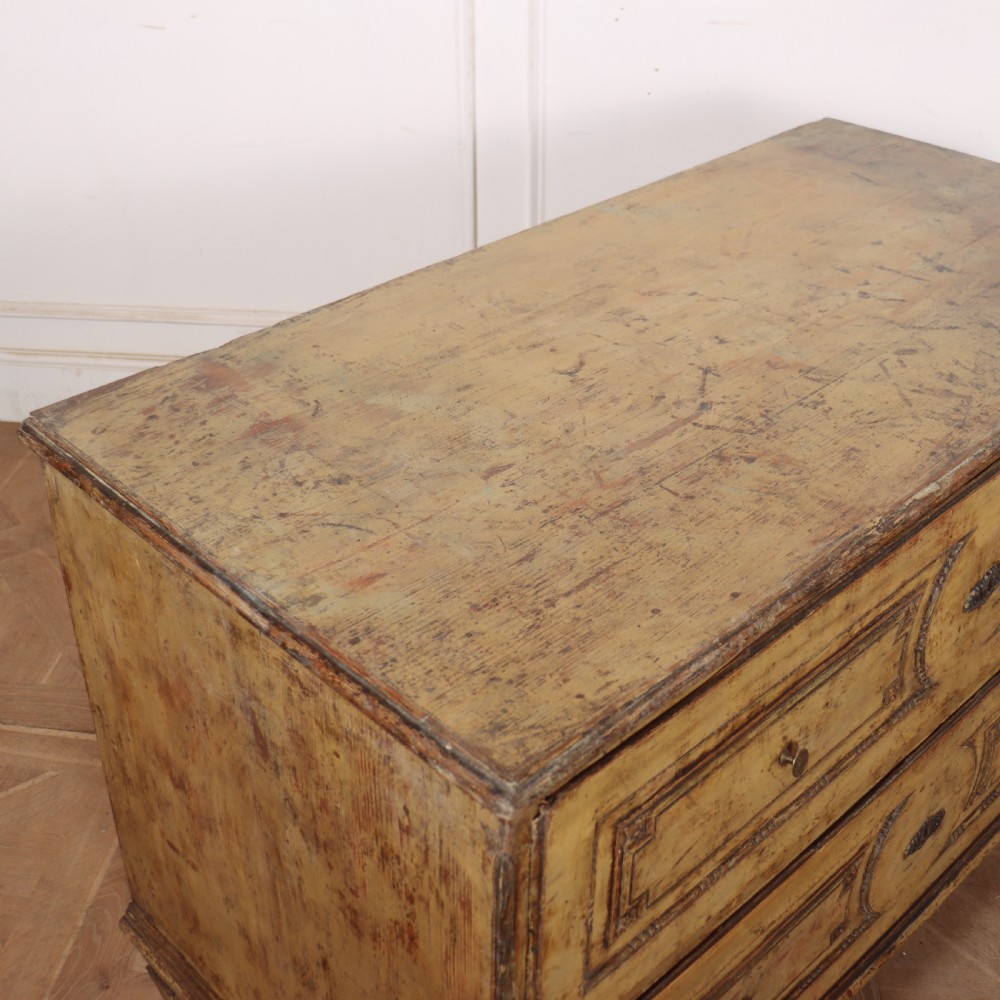 An antique two-drawer Italian commode with a muted yellow painted distressed finish, geometric panel mouldings, central brass escutcheons, and square tapered legs. View XI