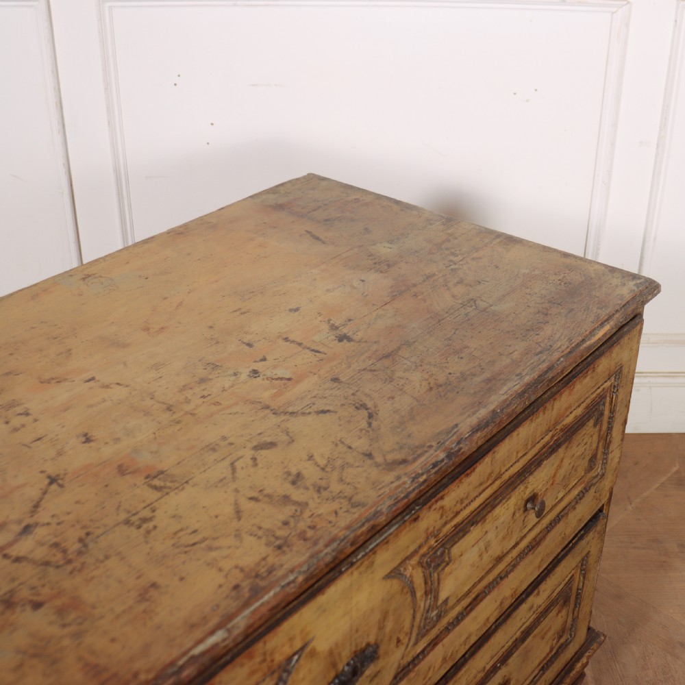 An antique two-drawer Italian commode with a muted yellow painted distressed finish, geometric panel mouldings, central brass escutcheons, and square tapered legs. View XII