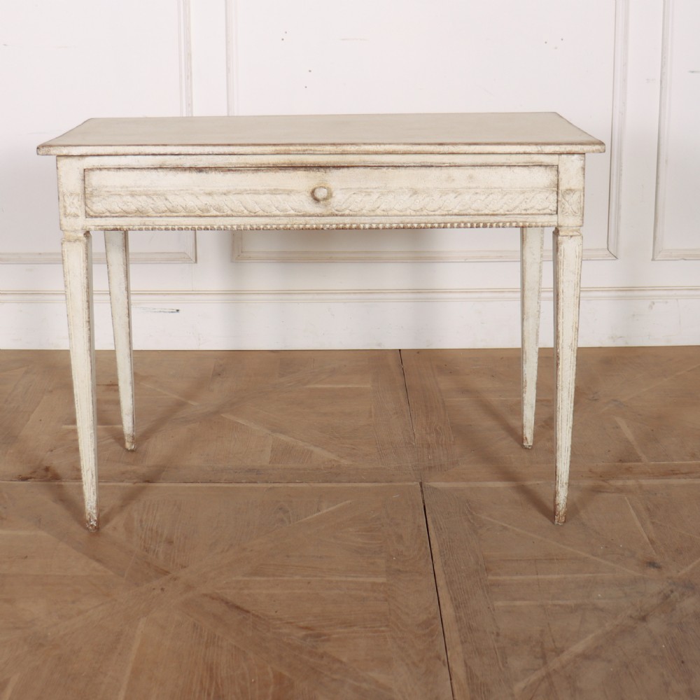 An antique off-white painted Swedish side table featuring tapered fluted legs, carved rope detail along the drawer frieze, and a single central drawer pull.