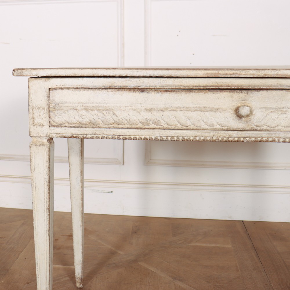 An antique off-white painted Swedish side table featuring tapered fluted legs, carved rope detail along the drawer frieze, and a single central drawer pull. View II