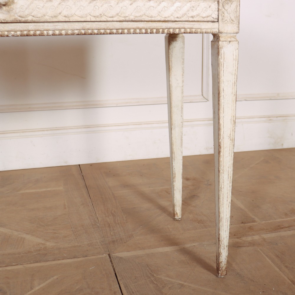An antique off-white painted Swedish side table featuring tapered fluted legs, carved rope detail along the drawer frieze, and a single central drawer pull. View IV