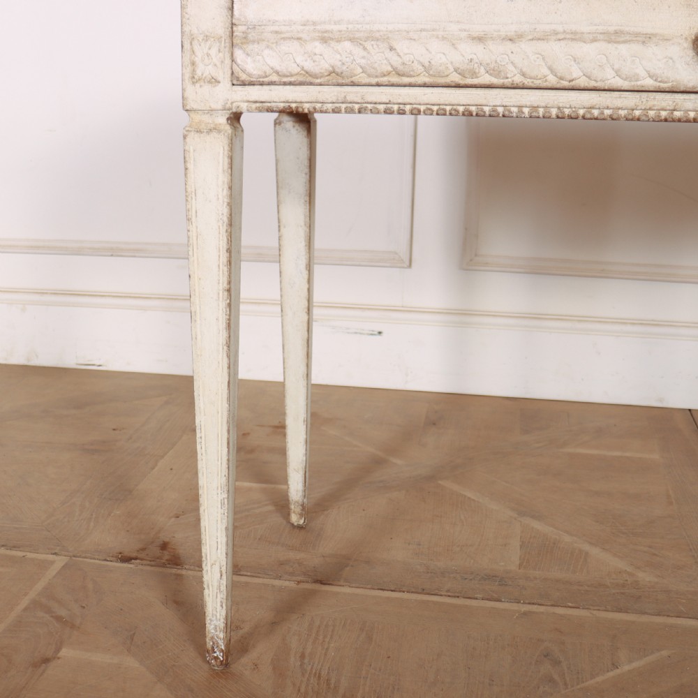 An antique off-white painted Swedish side table featuring tapered fluted legs, carved rope detail along the drawer frieze, and a single central drawer pull. View V