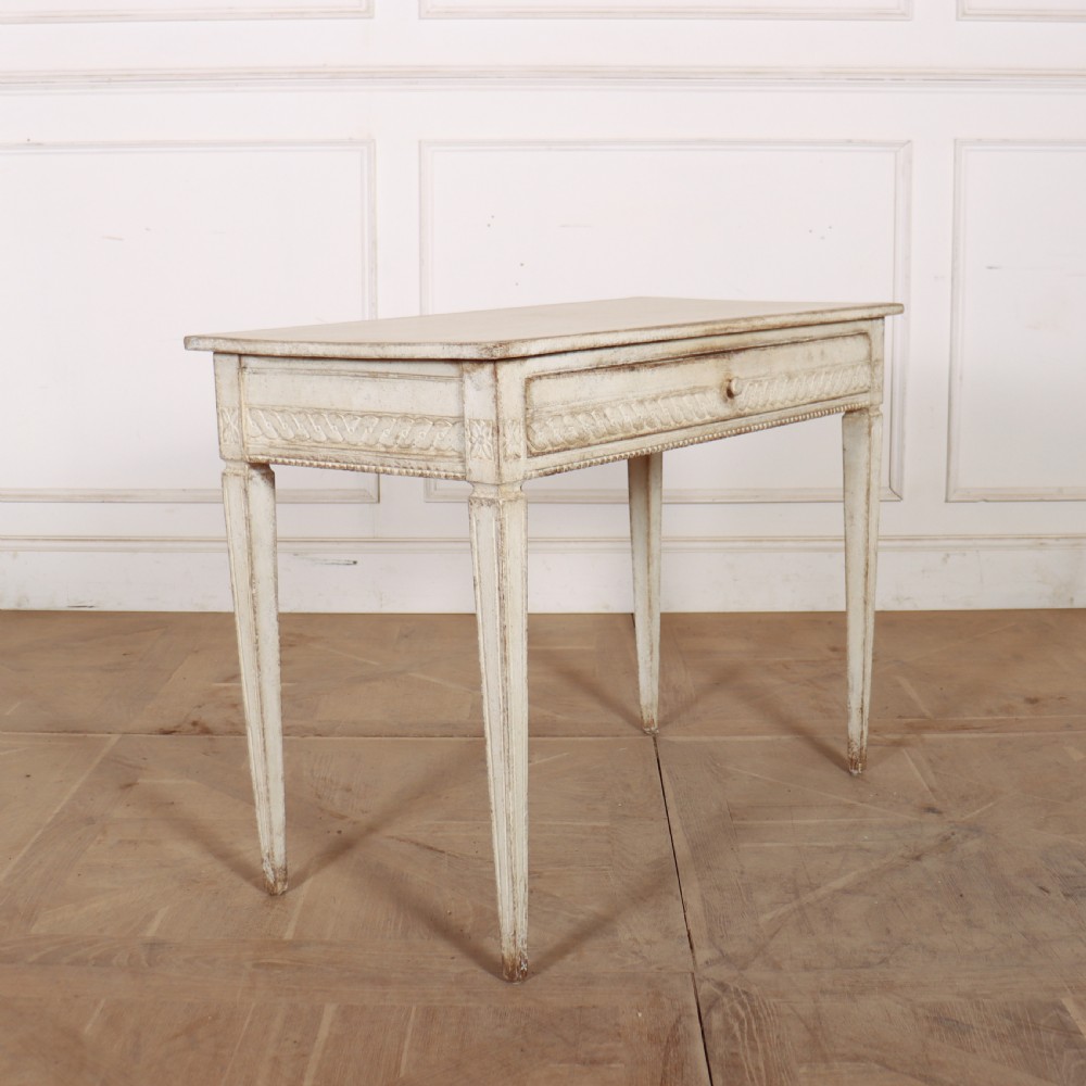 An antique off-white painted Swedish side table featuring tapered fluted legs, carved rope detail along the drawer frieze, and a single central drawer pull. View VI