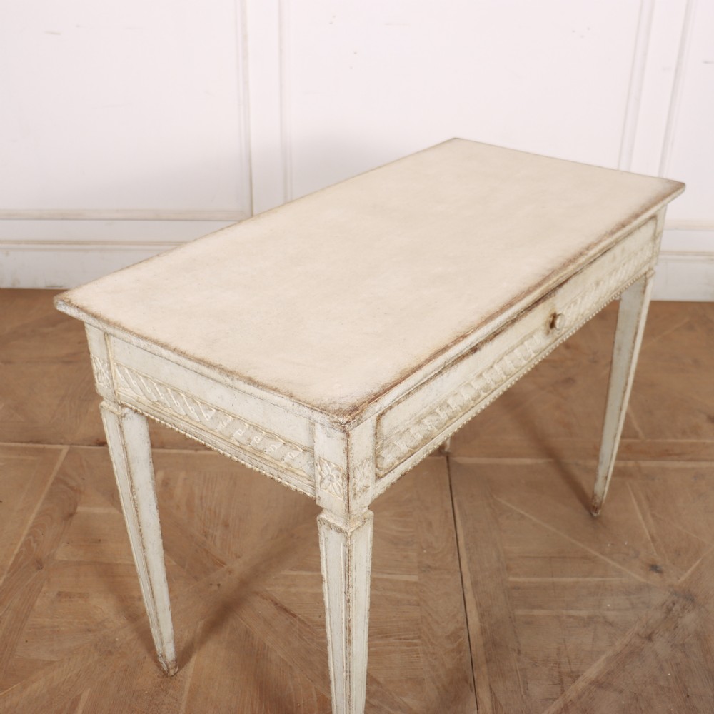 An antique off-white painted Swedish side table featuring tapered fluted legs, carved rope detail along the drawer frieze, and a single central drawer pull. View VIII