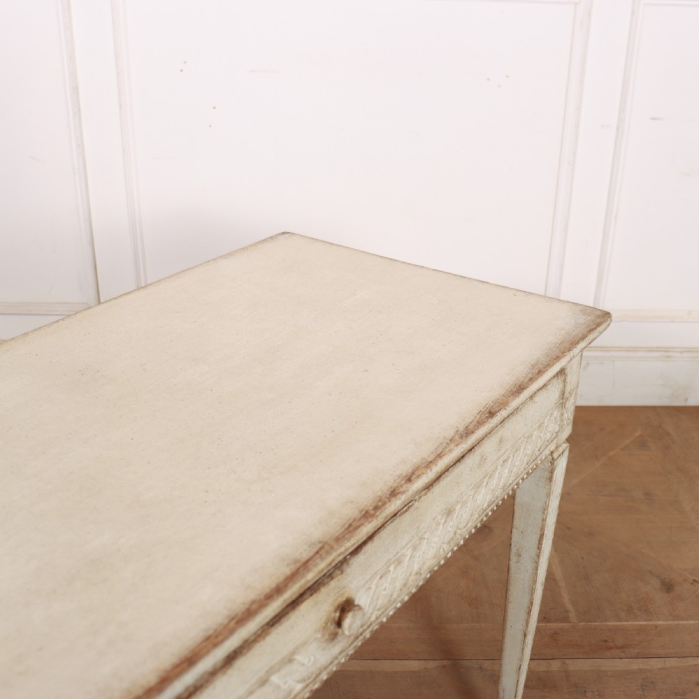 An antique off-white painted Swedish side table featuring tapered fluted legs, carved rope detail along the drawer frieze, and a single central drawer pull. View IX