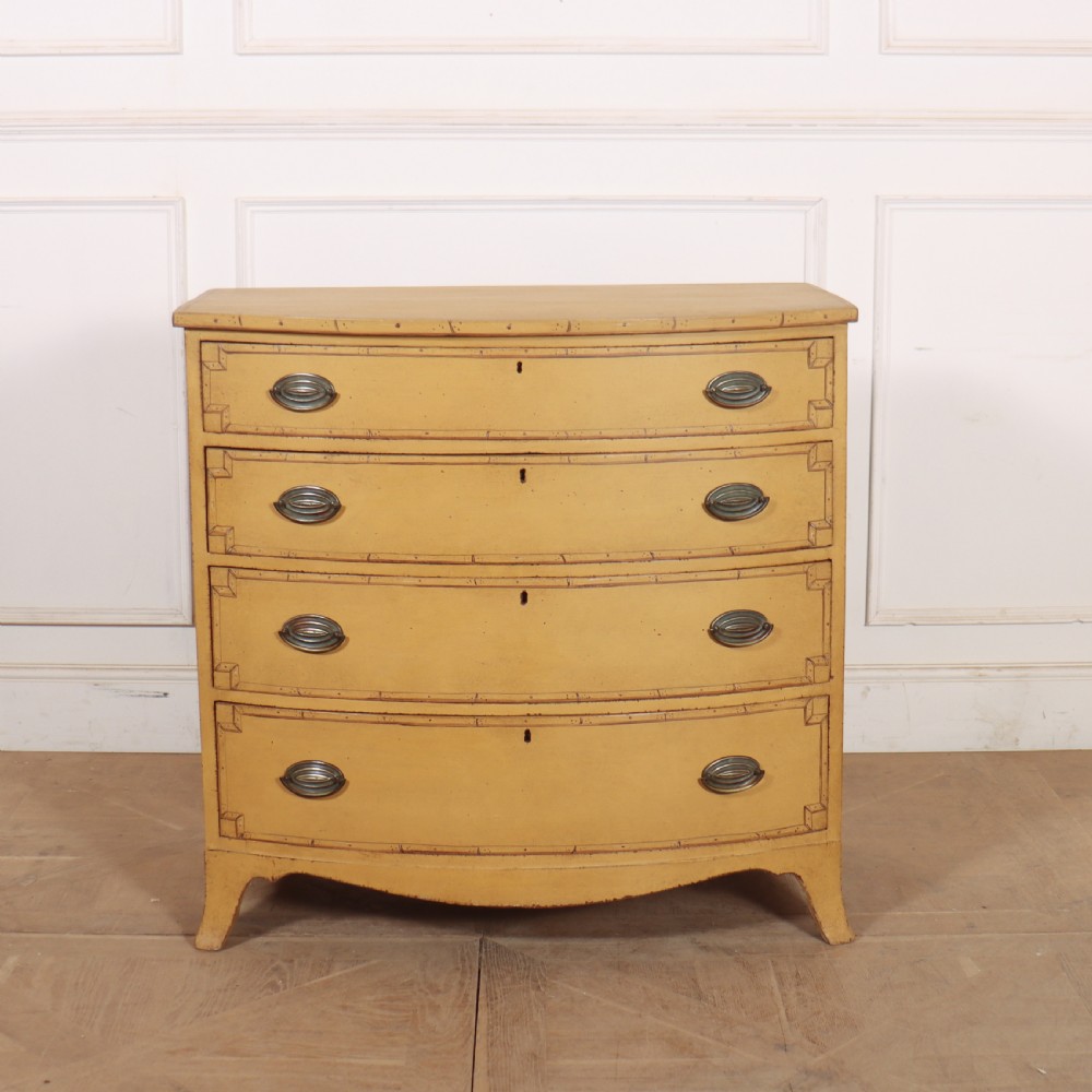 A Georgian bowfront chest of drawers with four graduated drawers painted in yellow with line borders and oval brass drop handles.