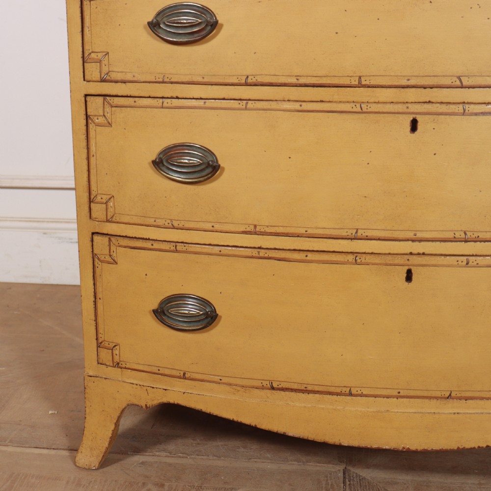 A Georgian bowfront chest of drawers with four graduated drawers painted in yellow with line borders and oval brass drop handles. View II