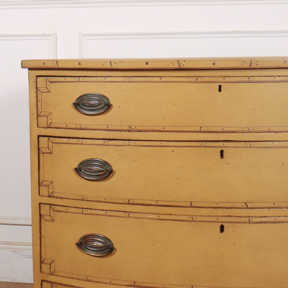 A Georgian bowfront chest of drawers with four graduated drawers painted in yellow with line borders and oval brass drop handles. View IV