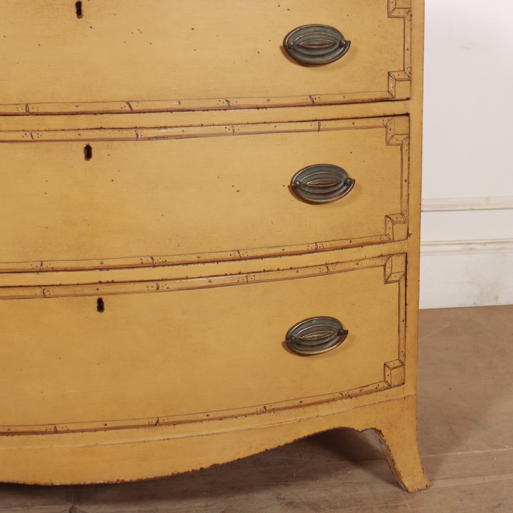 A Georgian bowfront chest of drawers with four graduated drawers painted in yellow with line borders and oval brass drop handles. View V