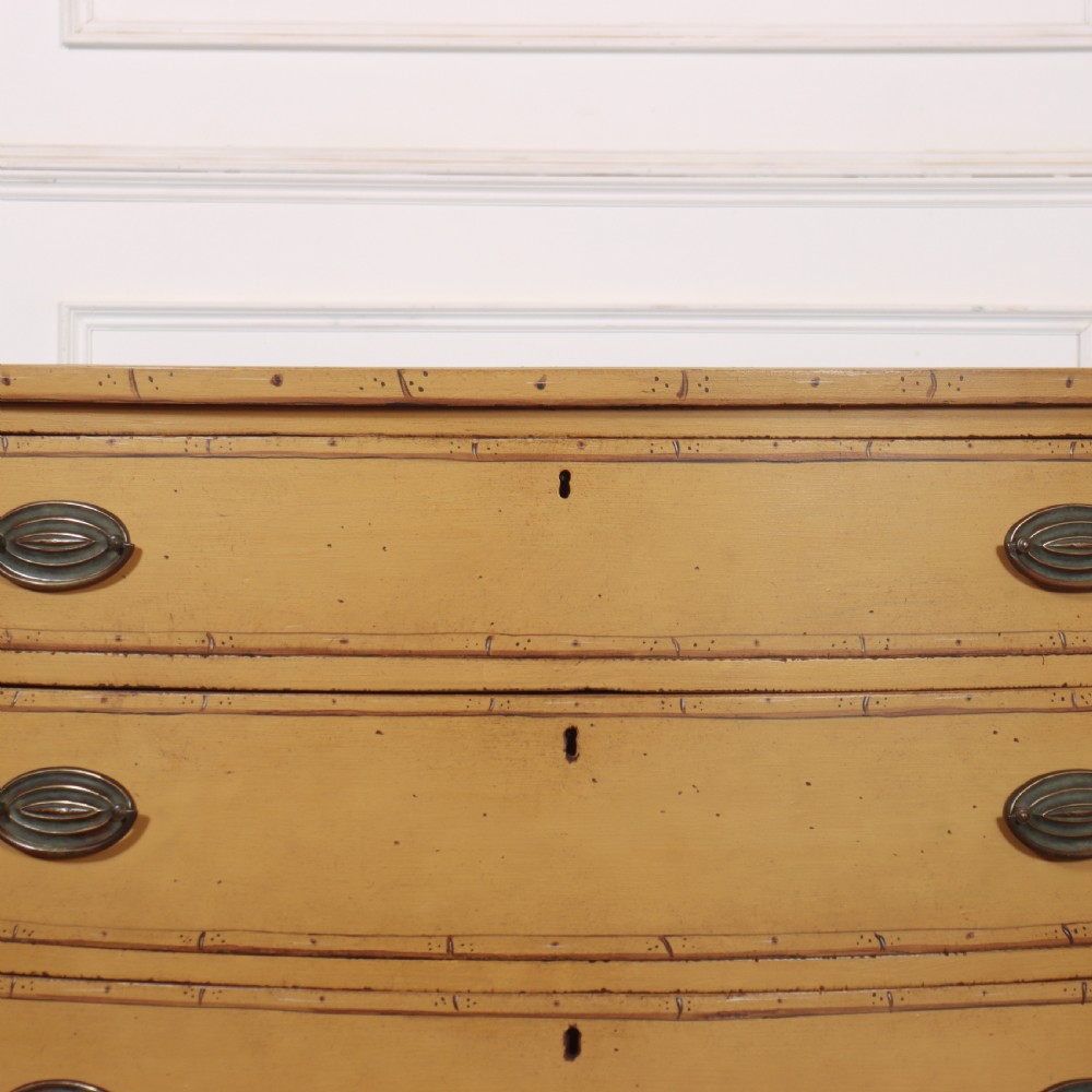 A Georgian bowfront chest of drawers with four graduated drawers painted in yellow with line borders and oval brass drop handles. View VI