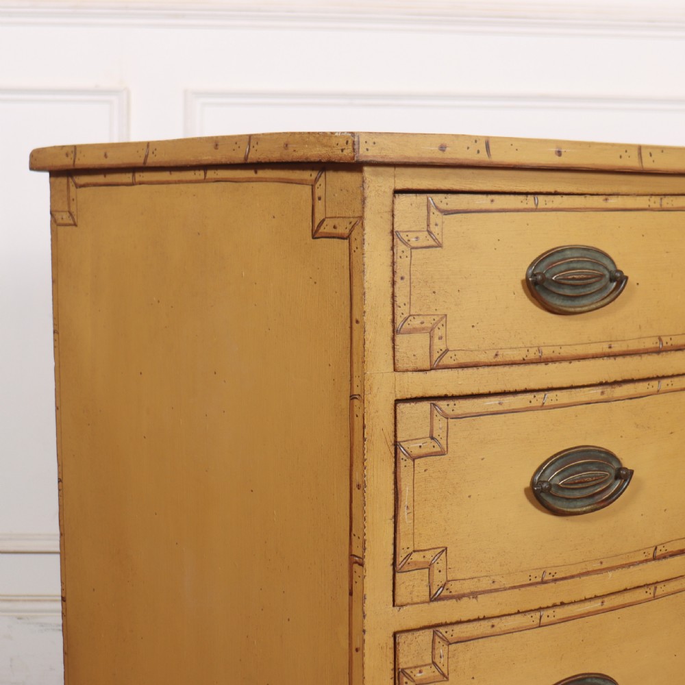 A Georgian bowfront chest of drawers with four graduated drawers painted in yellow with line borders and oval brass drop handles. View VIII