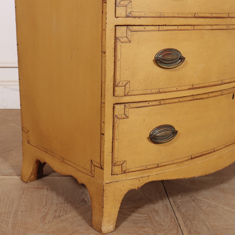 A Georgian bowfront chest of drawers with four graduated drawers painted in yellow with line borders and oval brass drop handles. View IX