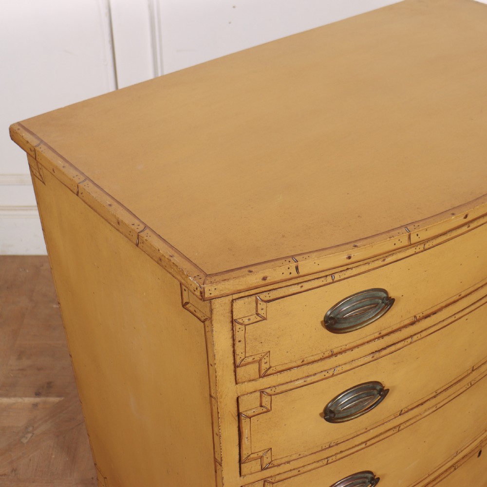 A Georgian bowfront chest of drawers with four graduated drawers painted in yellow with line borders and oval brass drop handles. View X