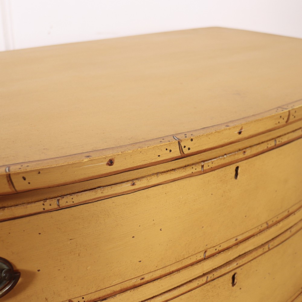 A Georgian bowfront chest of drawers with four graduated drawers painted in yellow with line borders and oval brass drop handles. View XI