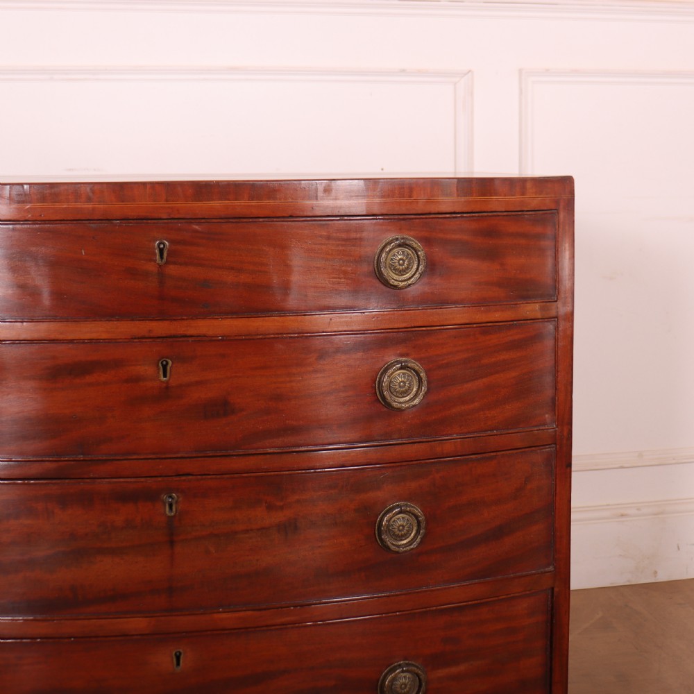 An antique mahogany bowfront chest of drawers featuring four graduated drawers with circular brass handles and splay bracket feet. View II