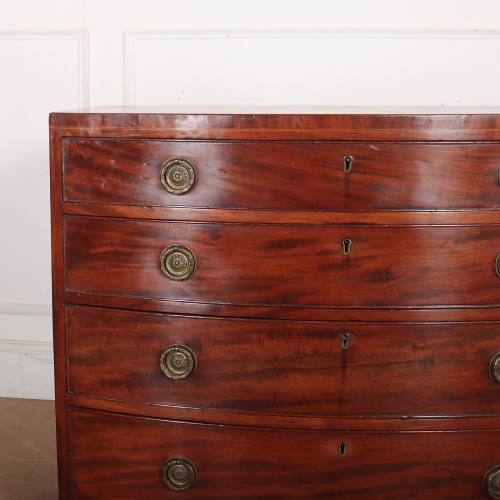 An antique mahogany bowfront chest of drawers featuring four graduated drawers with circular brass handles and splay bracket feet. View III