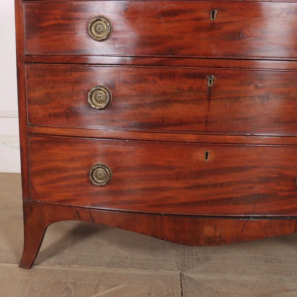 An antique mahogany bowfront chest of drawers featuring four graduated drawers with circular brass handles and splay bracket feet. View IV