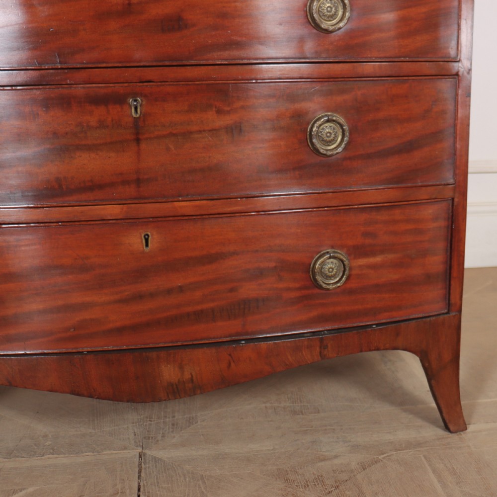 An antique mahogany bowfront chest of drawers featuring four graduated drawers with circular brass handles and splay bracket feet. View V