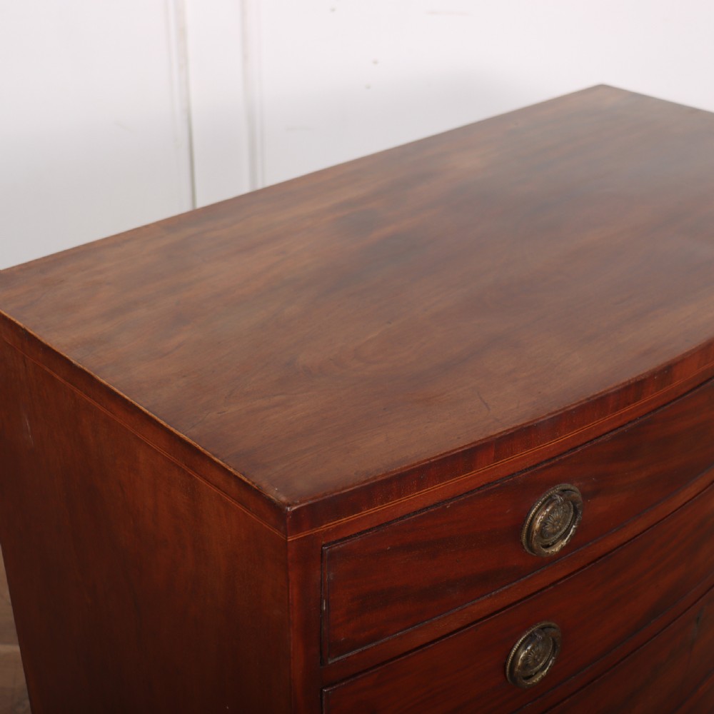 An antique mahogany bowfront chest of drawers featuring four graduated drawers with circular brass handles and splay bracket feet. View VI