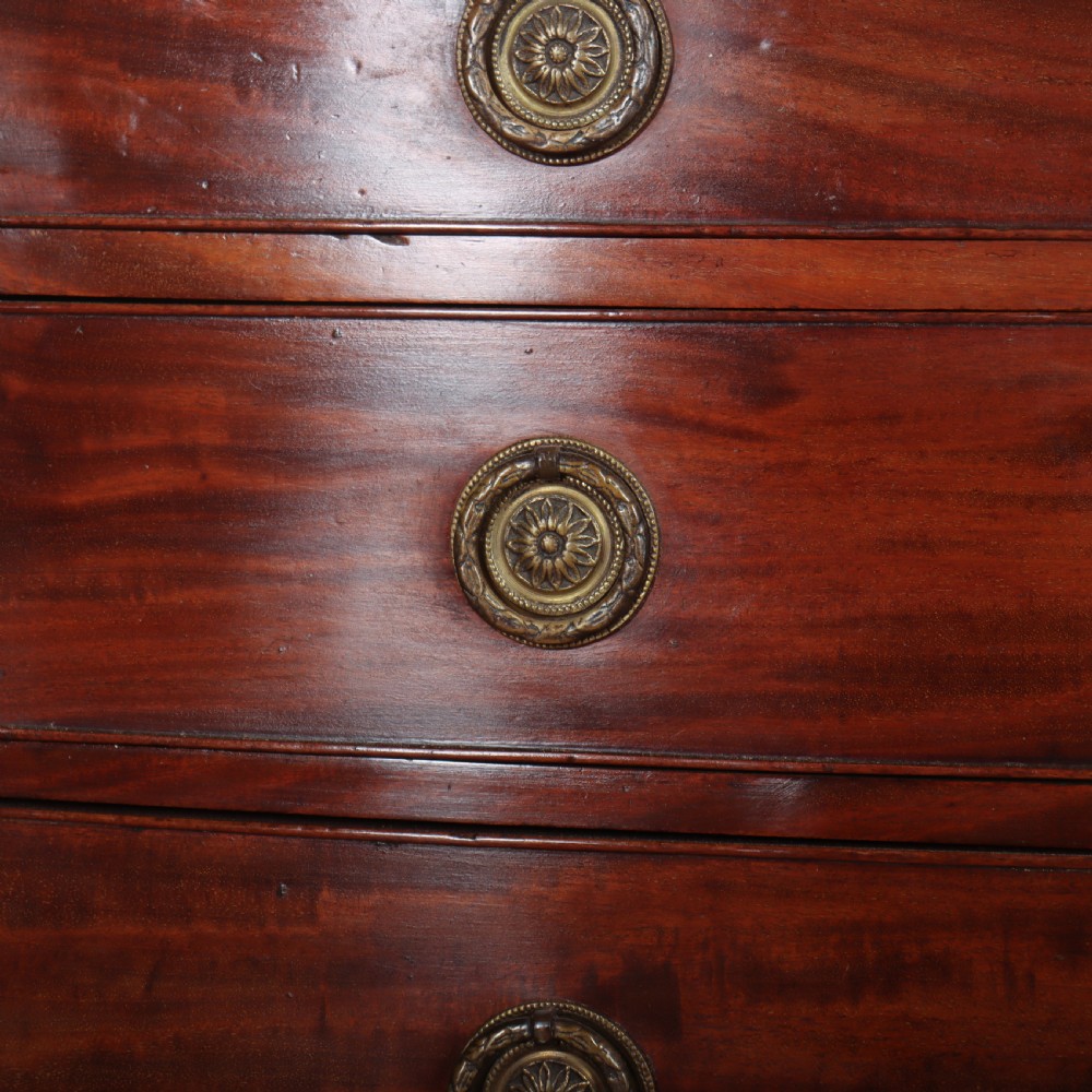 An antique mahogany bowfront chest of drawers featuring four graduated drawers with circular brass handles and splay bracket feet. View VII