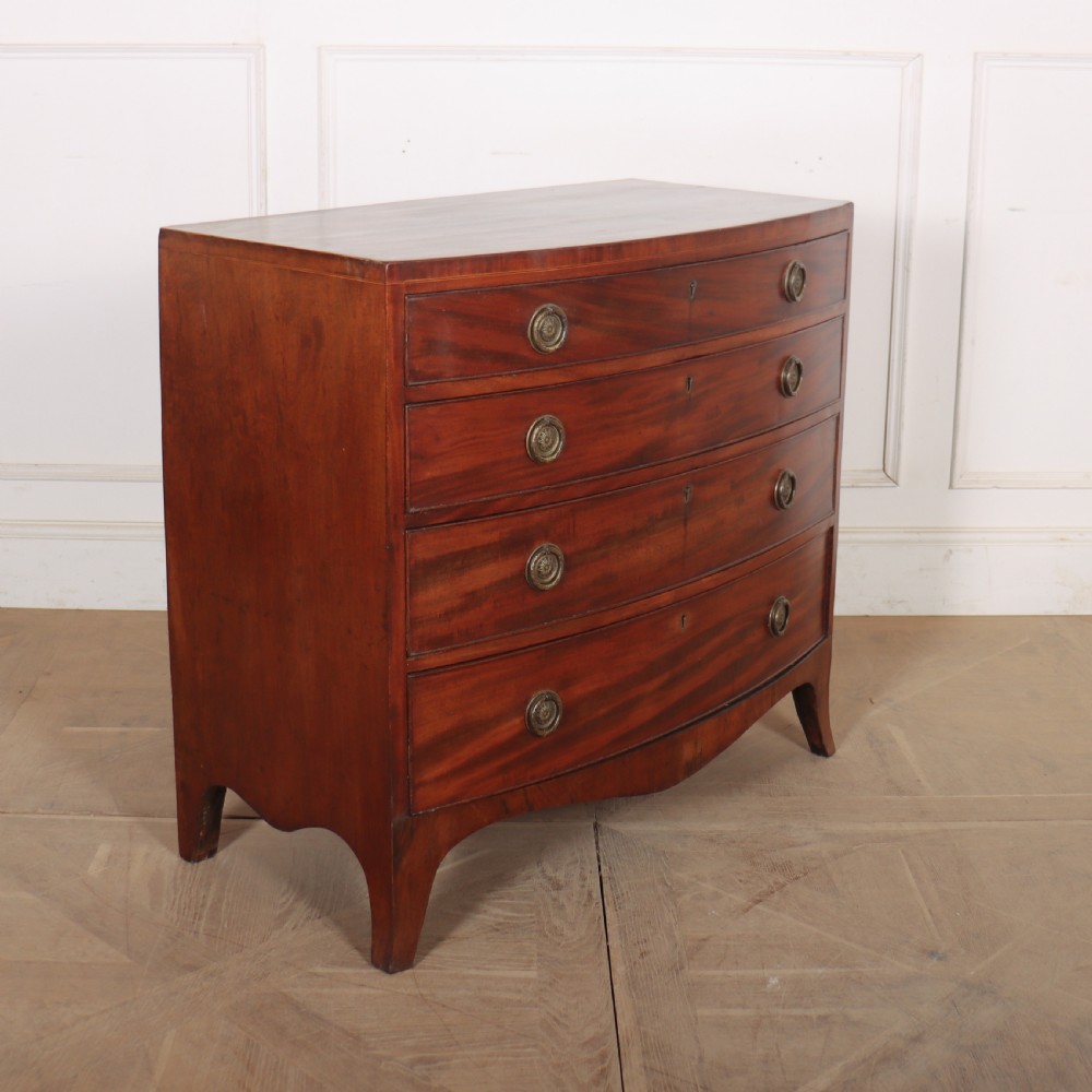 An antique mahogany bowfront chest of drawers featuring four graduated drawers with circular brass handles and splay bracket feet. View VIII