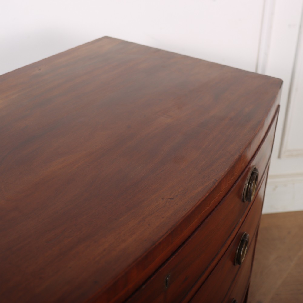 An antique mahogany bowfront chest of drawers featuring four graduated drawers with circular brass handles and splay bracket feet. View IX