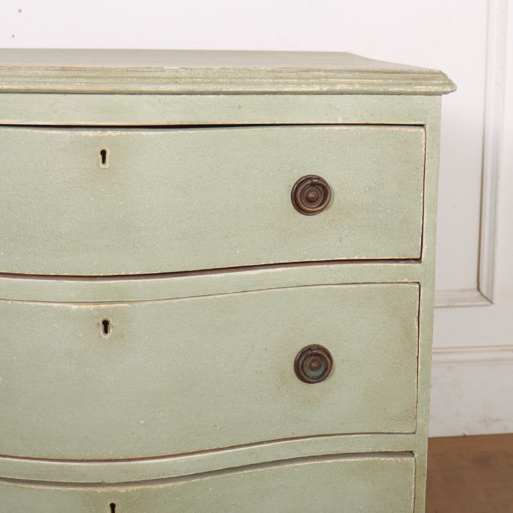 A Swedish serpentine painted commode featuring three drawers with brass pulls and a shaped apron in a muted green finish. View III