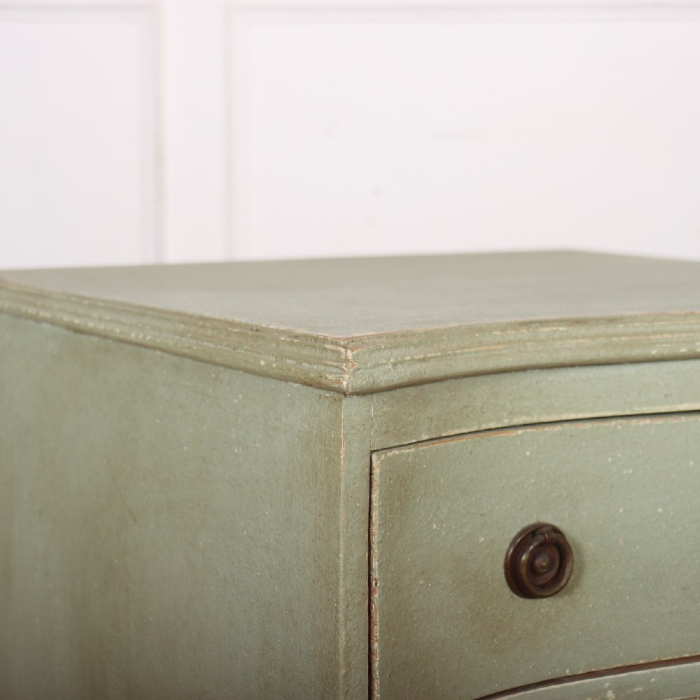 A Swedish serpentine painted commode featuring three drawers with brass pulls and a shaped apron in a muted green finish. View VII