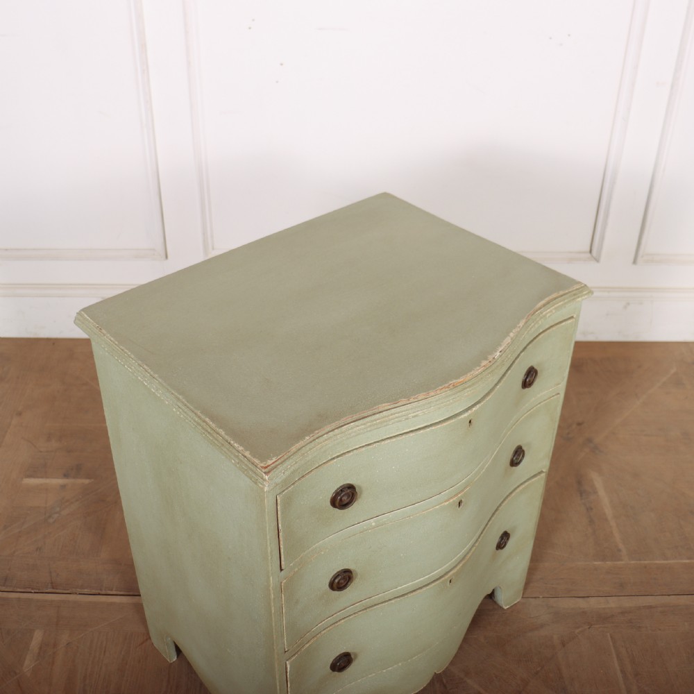 A Swedish serpentine painted commode featuring three drawers with brass pulls and a shaped apron in a muted green finish. View VIII